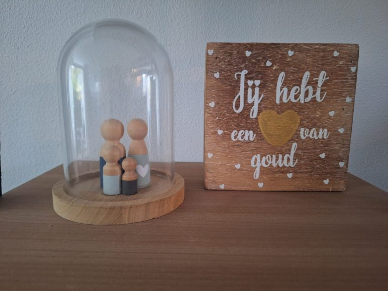 Houten poppetjes, familie, onder een glazen stolp naast een decoratieve tegel met een hart en tekst.