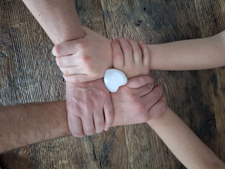 Verschillende handen die een hartvormige steen vasthouden op een houten oppervlak. Coach en therapeut.